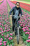 Young woman biking through tulip fields near Lisse, Netherlands, Europe