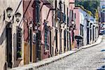 Woman walking on traditional cobblestone street carrying bag on head in San Miguel de Allende, Mexico