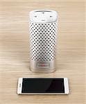 Silver smart speaker and smartphone on wood background