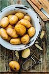 Peeled potatoes. Peeling a potato with peeler in a kitchen on a wooden rustic table. Top view