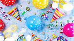 Bright colorful carnival or party pattern of balloons, streamers and confetti on blue table. Flat lay style, birthday or party greeting card and bokeh lights