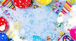 Bright colorful carnival or party scene frame of balloons, streamers and confetti on blue table. Flat lay style, birthday or party greeting card with copy space and bokeh lights