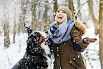 Woman walking her dog in the winter and both explore the snow together in playful mood