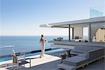 Woman on sunny modern, luxury home showcase exterior patio with ocean view