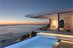 Illuminated modern, luxury home showcase exterior patio with lap pool and ocean view at twilight