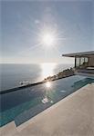 View of sun shining over ocean and modern, luxury home showcase exterior lap pool patio