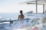 Serene woman meditating on modern, luxury home showcase exterior patio with ocean view