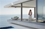 Woman talking on cell phone on modern, luxury home showcase exterior patio with ocean view