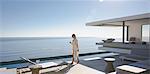 Woman walking on sunny, modern, luxury home showcase exterior patio with ocean view