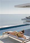 Woman sunbathing, texting with smart phone on lounge chair on sunny luxury patio with ocean view