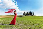 San Quirico d'Orcia, Orcia valley, Siena, Tuscany, Italy. A young woman in red dress relaxing in a wheat field near the cypresses of Orcia valley