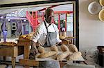 African baker carrying tray of loaves of bread in bakery