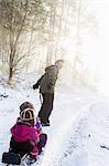 A father pulling his two young daughters on a sled