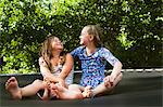 Two girls, sitting on trampoline on sunny day