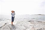 Boy standing on rocky seashore and looking through binoculars in the Stockholm archipelago