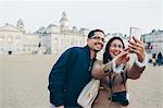 Mid adult man and woman taking selfies with London Horse Guards Parade in background
