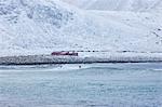 People surfing in the sea below snowy hills in Norway