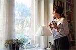 Woman looking through window, holding coffee cup