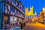 View of illuminated Lincoln Cathedral viewed from Exchequer Gate with timbered architecture of Visitors Centre at dusk, Lincoln, Lincolnshire, England, United Kingdom, Europe