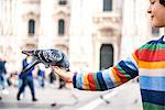 Boy feeding pigeon on hand in square, Milan, Lombardy, Italy