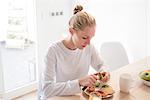 Young woman peeling kiwi fruit at breakfast table