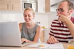 Young woman and boyfriend doing paperwork and using laptop at table