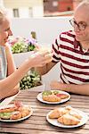 Young woman handing breakfast orange juice to boyfriend at patio table