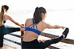 Two young women training on sea waterfront, touching toes