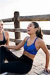 Two young women training on waterfront, sitting laughing