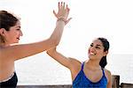 Two young women training together on sea waterfront, high fiving