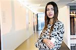 Portrait of confident young businesswoman holding smartphone in office corridor