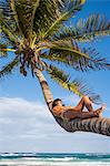 Young woman sunbathing on palm tree trunk at beach, Tulum, Quintana Roo, Mexico