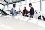 Car salesman giving car keys to customers in car dealership showroom