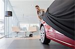 Car saleswoman removing cover from new car in car dealership showroom