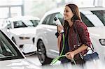 Smiling female customer carrying hybrid charging cable in car dealership showroom