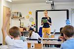 Schoolboy with hand raised in classroom lesson at primary school