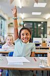 Schoolgirl with hand up in classroom at primary school