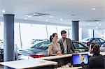 Couple customers talking to male receptionist at desk in car dealership showroom