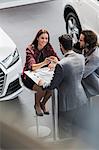 Car salesman giving car keys to smiling female customer in car dealership showroom