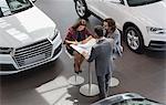 Car salesman watching couple customers signing financial contract paperwork in car dealership showroom