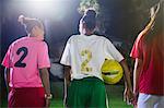 Young female soccer players with ball talking on field at night