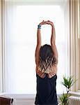 Woman practicing yoga, stretching arms overhead at window