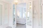 White, luxury home showcase interior bedroom with French doors and chandelier