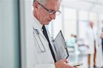 Male doctor with clipboard texting with smart phone in hospital