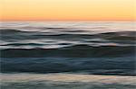 Seascape with breaking waves under cloudy sky at sunset.