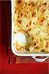 Baked scalloped potatoes and sweet potatoes in a casserole dish on a red background