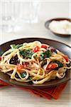 Linguine pasta with tomato, leafy greens and crushed red pepper on dark brown plate