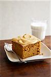 Pumpkin cake square with icing on a plate with a glass of milk