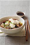 Tofu in broth with shiitake mushrooms, green onions and cabbage served with soy sauce and chopsticks