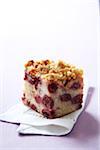 Slice of cherry coffee cake with crumble topping on a white napkin